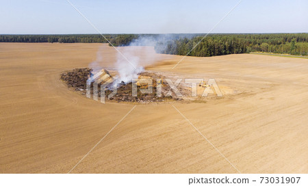 Excavators clear the field from the forest to increase farmland. Burning trees in a pit after increasing the plowed field. Inefficient farming. The burning of the forest. Environmental problem. Excavators clear the field from the forest to increase farmland. Burning trees in a pit after increasing the plowed field. Inefficient farming. The burning of the forest. Environmental problem. 73031907