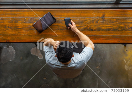 High angle view of Asian man using cellphone and tablet High angle view of Asian man using cellphone and tablet 73033199