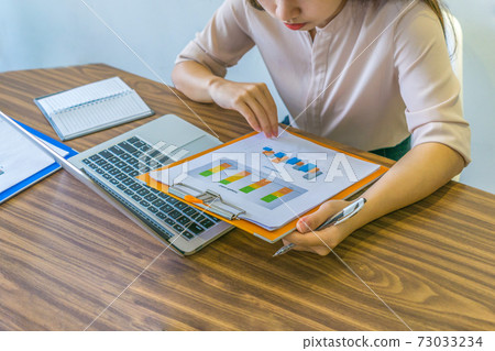Asian office employee checking sales statistics report at workplace Asian office employee checking sales statistics report at workplace 73033234