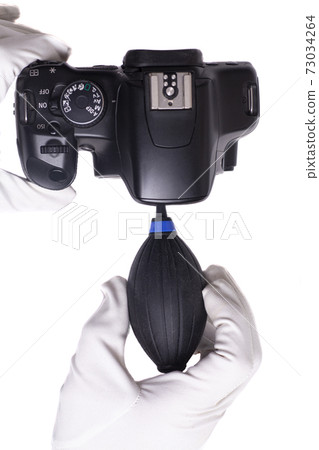 Hand wearing white gloves cleaning camera with air dust blower. Hand wearing white gloves cleaning camera with air dust blower. 73034264