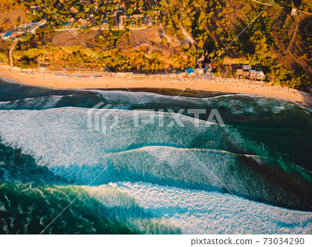 Aerial view of coastline at warm sunset and Bali beach. Perfect ocean waves for surfing Aerial view of coastline at warm sunset and Bali beach. Perfect ocean waves for surfing 73034290