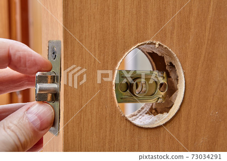 The carpenter replaces the door lock. Hole for handles into the wood interior door and brass latch. The carpenter replaces the door lock. Hole for handles into the wood interior door and brass latch. 73034291