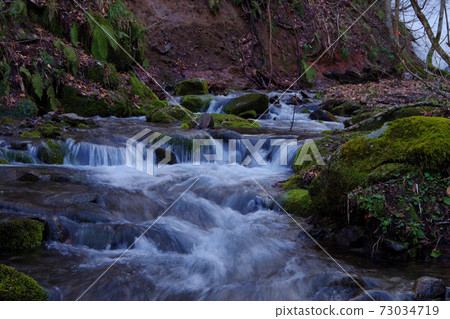A clear stream flowing between moss stones in a mountain stream 73034719