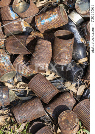 Old rusty cans lie on the ground and dry grass in nature. Old rusty cans lie on the ground and dry grass in nature. 73035565