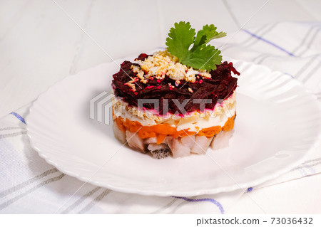 Traditional Russian herring under a fur coat on white plate with parsley. Rustic style. Christmas russian salad. 73036432