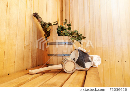 Interior details Finnish sauna steam room with traditional sauna accessories basin birch broom scoop felt hat towel. Traditional old Russian bathhouse SPA Concept. Relax country village bath concept. Interior details Finnish sauna steam room with traditional sauna accessories basin birch broom scoop felt hat towel. Traditional old Russian bathhouse SPA Concept. Relax country village bath concept. 73036626
