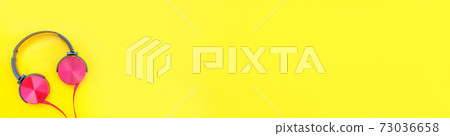 Red headphones on yellow background. Minimalist simple photo of earphones with copy space, banner. Red dj headphones with cable isolated on colorful backdrop, flat lay top view. Music concept. 73036658