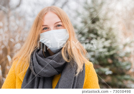 Young blond woman wearing white medical face mask over nature background, trendy colors of year 2021 - illuminatiing yellow and ultimate gray. COVID-19 Pandemic Coronavirus Young blond woman wearing white medical face mask over nature background, trendy colors of year 2021 - illuminatiing yellow and ultimate gray. COVID-19 Pandemic Coronavirus 73038498