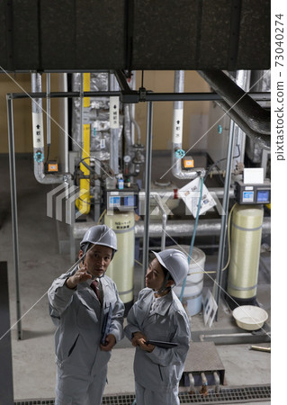 Workers performing equipment maintenance at factory facilities 73040274