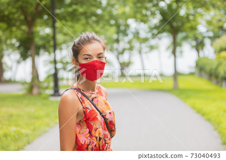 Asian woman wearing facial covering walking on street while waiting outside bus stop for public transport. Summer fashion portrait in red mask Asian woman wearing facial covering walking on street while waiting outside bus stop for public transport. Summer fashion portrait in red mask 73040493