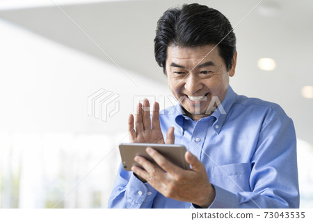 朝他的智能手機屏幕揮舞著的高級男人微笑著 朝他的智能手機屏幕揮舞著的高級男人微笑著 73043535