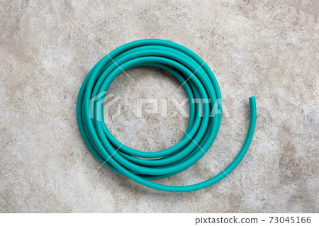 Green garden hose on cement floor background. Green garden hose on cement floor background. 73045166