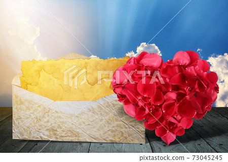 heart shape made out of rose petals with old letter on wooden deck table 73045245