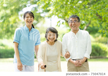 Senior couple and caregiver taking a walk 73047814