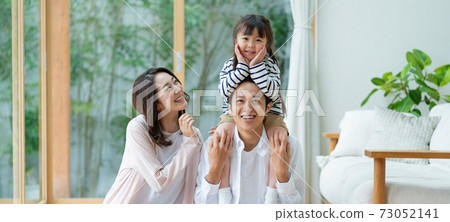 A portrait of a family of three, a girl sitting in the living room, being piggybacked by her dad, and a dad and mom. 73052141