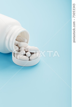 White capsules with vitamins and minerals in the form are poured from a jar on a blue background. 73053343
