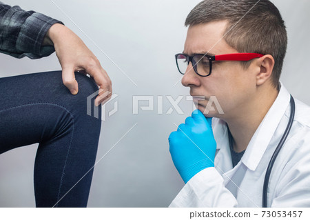 A woman suffers from knee pain. Examination by an orthopedist and traumatologist. Redness and swelling of the legs, torn meniscus or knee bursitis. The doctor examines 73053457