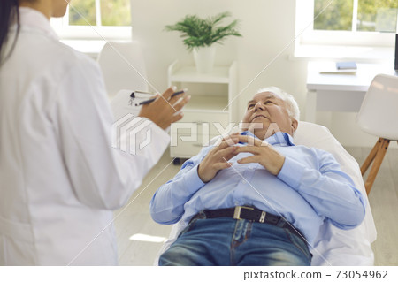 Senior patient listening to doctor lying on bed in hospital office during medical check-up Senior patient listening to doctor lying on bed in hospital office during medical check-up 73054962