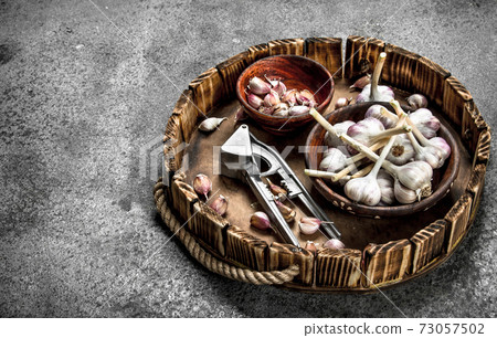 Fresh garlic in bowls with a press tool on a wooden tray. Fresh garlic in bowls with a press tool on a wooden tray. 73057502