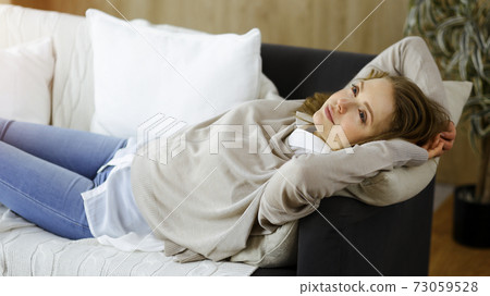 Happy blond woman put hands behind head sitting leaned on couch caucasian female enjoy lazy weekend or vacation in sunny living room 73059528