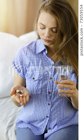 Young woman holding pills time to take medications, cure for headache, high blood pressure or cholesterol level remedy pain killer drugs Young woman holding pills time to take medications, cure for headache, high blood pressure or cholesterol level remedy pain killer drugs 73059554
