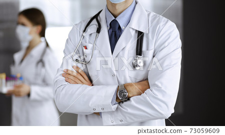 Unknown male doctor in protective mask standing with arms crossed in clinic. Medicine concept during Coronavirus pandemic. Covid 2019 73059609