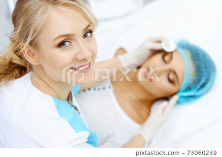 Professional beautician and young woman in beauty salon. Makeup artist touch customer skin with cotton pads, closeup. Cosmetology , facial, beauty and spa Professional beautician and young woman in beauty salon. Makeup artist touch customer skin with cotton pads, closeup. Cosmetology , facial, beauty and spa 73060239