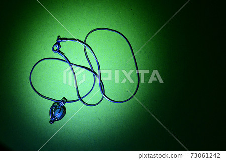 Pendant with a pearl and a chain on a green background. 73061242