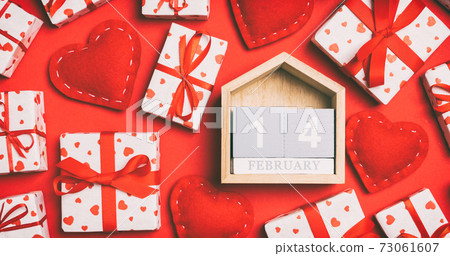 Top view of wooden calendar, white gift boxes and red textile hearts on colorful background. Valentine's Day concept 73061607