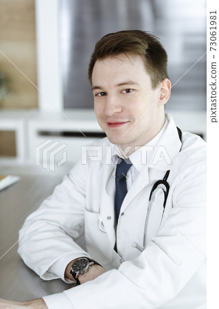 Doctor man sitting behind a computer at workplace in clinic or hospital office. Medic headshot and medicine concept Doctor man sitting behind a computer at workplace in clinic or hospital office. Medic headshot and medicine concept 73061981