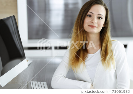 Business woman headshot at workplace in modern office. Unknown businesswoman sitting behind computer monitor. Young accountant or secretary looks good Business woman headshot at workplace in modern office. Unknown businesswoman sitting behind computer monitor. Young accountant or secretary looks good 73061983