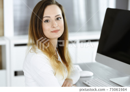 Business woman headshot at workplace in modern office. Unknown businesswoman sitting behind computer monitor. Young accountant or secretary looks good Business woman headshot at workplace in modern office. Unknown businesswoman sitting behind computer monitor. Young accountant or secretary looks good 73061984