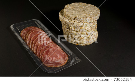 Grain crispbreads crispy rice and diet bread with smoked sausage. Rice cake puffed rice with salami, sausage, balyk, smoked meat on black background Grain crispbreads crispy rice and diet bread with smoked sausage. Rice cake puffed rice with salami, sausage, balyk, smoked meat on black background 73062194