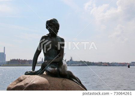 A tourist attraction in Copenhagen, Denmark, a mermaid princess with a somewhat melancholy look sitting on a stone 73064261