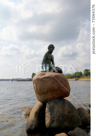 A tourist attraction in Copenhagen, Denmark, a mermaid princess sitting on a large stone, vertical position 73064376
