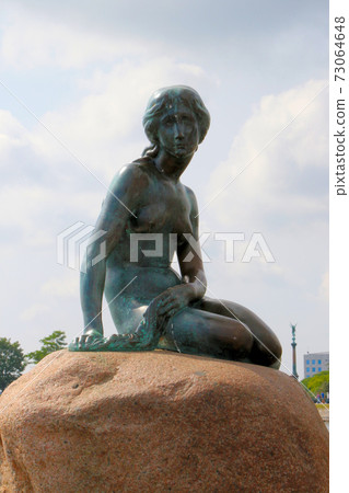 A tourist attraction in Copenhagen, Denmark, a mermaid princess with a melancholy look in the bright sky, vertical position 73064648