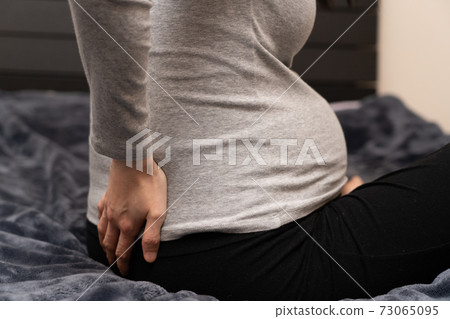 Pregnant woman putting her hand on her back 73065095