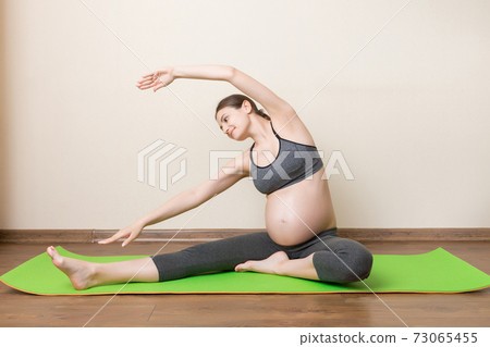 Pregnancy Yoga and Fitness concept at coronavirus time. Pregnant woman meditates indoor in yoga pose. Woman enjoying in meditation 73065455