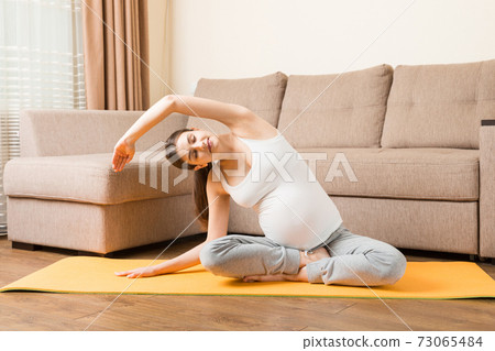 beautiful young pregnant woman sitting near sofa in yoga pose at the home. Pregnancy Yoga and Fitness concept at coronavirus time 73065484