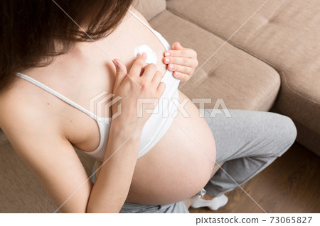 pregnant woman applying stretch mark cream to belly. pregnancy, people and maternity concept. pregnant apply anti-stretch mark cream on her breast pregnant woman applying stretch mark cream to belly. pregnancy, people and maternity concept. pregnant apply anti-stretch mark cream on her breast 73065827