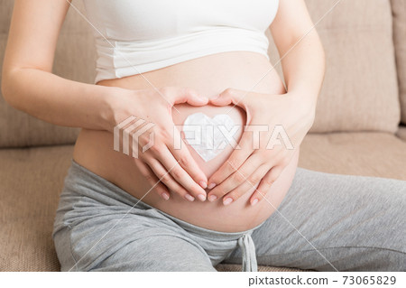 a pregnant girl sits at home on the bed and smears heart an anti-stretch mark cream on her stomach. Pregnancy, motherhood, preparation and expectation concept a pregnant girl sits at home on the bed and smears heart an anti-stretch mark cream on her stomach. Pregnancy, motherhood, preparation and expectation concept 73065829