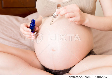 a pregnant girl sits at home on the bed and smears smile an anti-stretch mark cream on her stomach. Pregnancy, motherhood, preparation and expectation concept a pregnant girl sits at home on the bed and smears smile an anti-stretch mark cream on her stomach. Pregnancy, motherhood, preparation and expectation concept 73065875