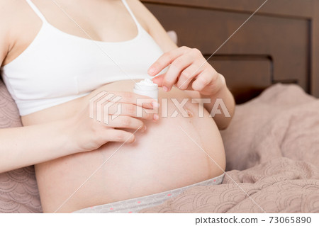 pregnant woman applying stretch mark cream to belly. pregnancy, people and maternity concept. pregnant apply anti-stretch mark cream on her belly pregnant woman applying stretch mark cream to belly. pregnancy, people and maternity concept. pregnant apply anti-stretch mark cream on her belly 73065890