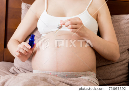 a pregnant girl sits at home on the bed and smears smile an anti-stretch mark cream on her stomach. Pregnancy, motherhood, preparation and expectation concept a pregnant girl sits at home on the bed and smears smile an anti-stretch mark cream on her stomach. Pregnancy, motherhood, preparation and expectation concept 73065892