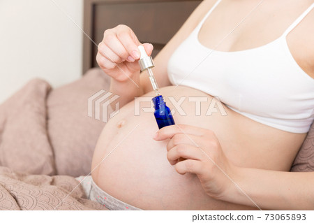 pregnant woman applying stretch mark cream to belly. pregnancy, people and maternity concept. pregnant apply anti-stretch mark cream on her belly pregnant woman applying stretch mark cream to belly. pregnancy, people and maternity concept. pregnant apply anti-stretch mark cream on her belly 73065893