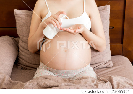 pregnant woman applying stretch mark cream to belly. pregnancy, people and maternity concept. pregnant apply anti-stretch mark cream on her belly 73065905