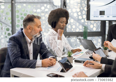 Two business partners, young African woman and senior Caucasian man, working with new ideas about project in conference room. Business people discussing over new business project in office. Two business partners, young African woman and senior Caucasian man, working with new ideas about project in conference room. Business people discussing over new business project in office. 73065982