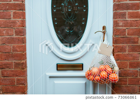 Reusable string bag from environmentally friendly materials with citrus fruits and blank card hanging on the door handle. Local farmer healthy food delivery. Zero-waste, plastic-free lifestyle Reusable string bag from environmentally friendly materials with citrus fruits and blank card hanging on the door handle. Local farmer healthy food delivery. Zero-waste, plastic-free lifestyle 73066861