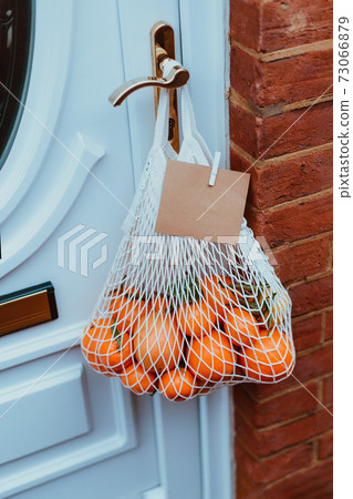 Reusable string bag from environmentally friendly materials with citrus fruits and blank card hanging on the door handle. Local farmer healthy food delivery. Zero-waste, plastic-free lifestyle. Reusable string bag from environmentally friendly materials with citrus fruits and blank card hanging on the door handle. Local farmer healthy food delivery. Zero-waste, plastic-free lifestyle. 73066879
