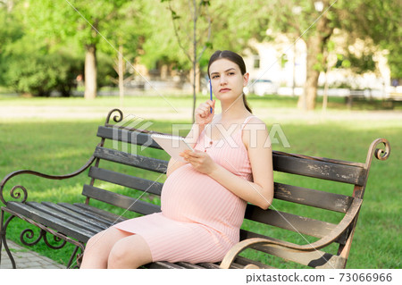 pregnant woman sits on a park bench and writes a to do list to the hospital 73066966